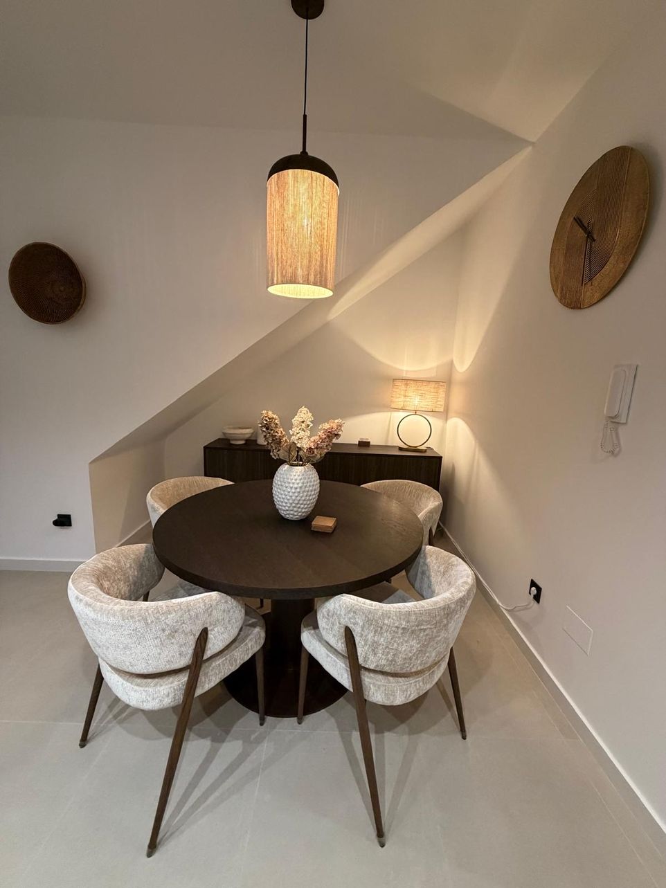 Ronde donkere eettafel met vier gestoffeerde stoelen onder een rieten hanglamp
